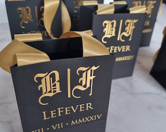 Op de afbeelding: Zwarte cadeauzakken met gouden lintjes en gouden letters. De zakken hebben de initialen "B|F" en de naam "LEFEVER" met de datum "XII.VII.MMXXXIV".