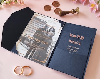 May include: A navy blue wedding invitation with a gold border and a black and white photo of the couple. The invitation includes the couple's names, the date of the wedding, and the location. The RSVP card is also included, with details about the attire and cocktail hour.