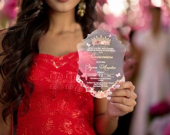 May include: A clear acrylic Quinceañera invitation with a pink and gold floral design. The invitation features a crown, butterflies, and the text "Quinceañera" in gold lettering. The text on the invitation reads: "Slyana Ampatie, Saturday October 12, 2024, 1:00PM, St. Peter the Apostle Catholic Church, 1301 & Cherry Lane."