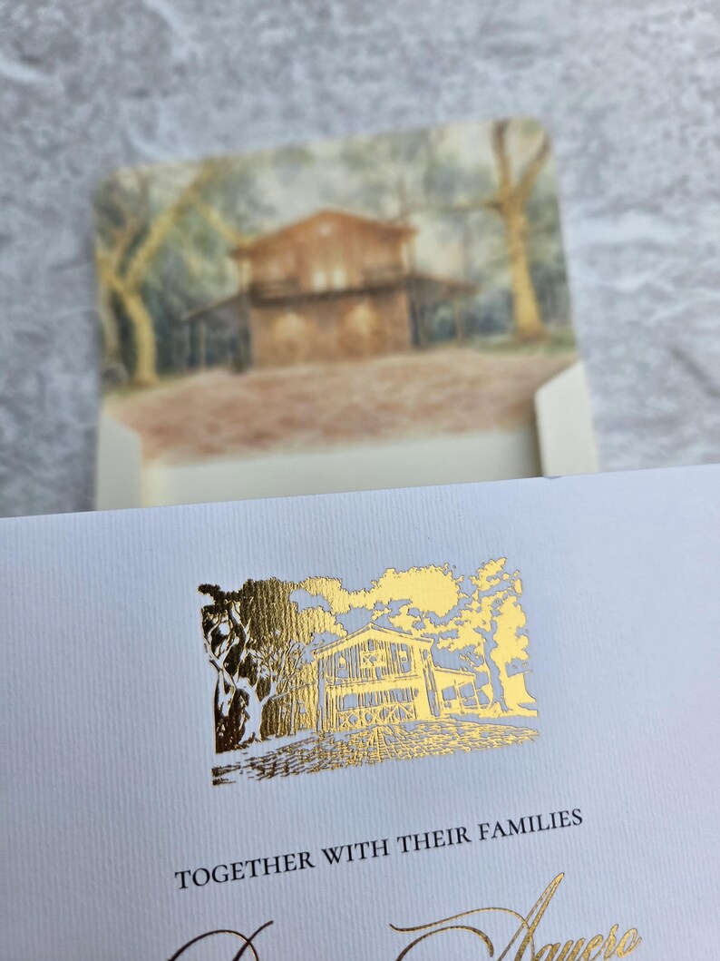 K&ouml;nnte beinhalten: Cremefarbene Einladung mit goldfarbenen Akzenten. Das Design zeigt eine detaillierte Illustration eines Hauses und B&auml;ume. Der Text "TOGETHER WITH THEIR FAMILIES" ist unter der Illustration gedruckt. Der Umschlag hat ein Aquarellgem&auml;lde des Hauses.