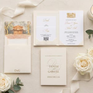 K&ouml;nnte beinhalten: Elegante Hochzeitseinladungssuite in Creme und Gold. Enth&auml;lt Einladungskarten, RSVP-Karten und eine Pocketfold-Karte mit einer Aquarell-Scheunen-Szene. Mit den Namen "Denise und Gabriel" und dem Datum "11. April 2026". Enth&auml;lt wei&szlig;e Rosen und eine brennende Kerze.