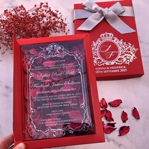 Invito nozze in scatola rossa personalizzata con stampa argento, nastro argento e petali di rosa rossi.