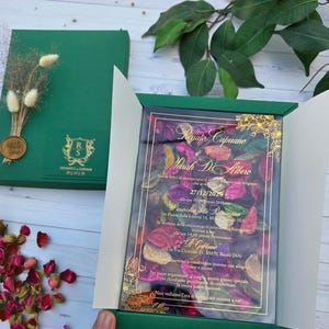 Boîte vert émeraude avec invitation en acrylique, fleurs, pétales de rose et sceau personnalisé.