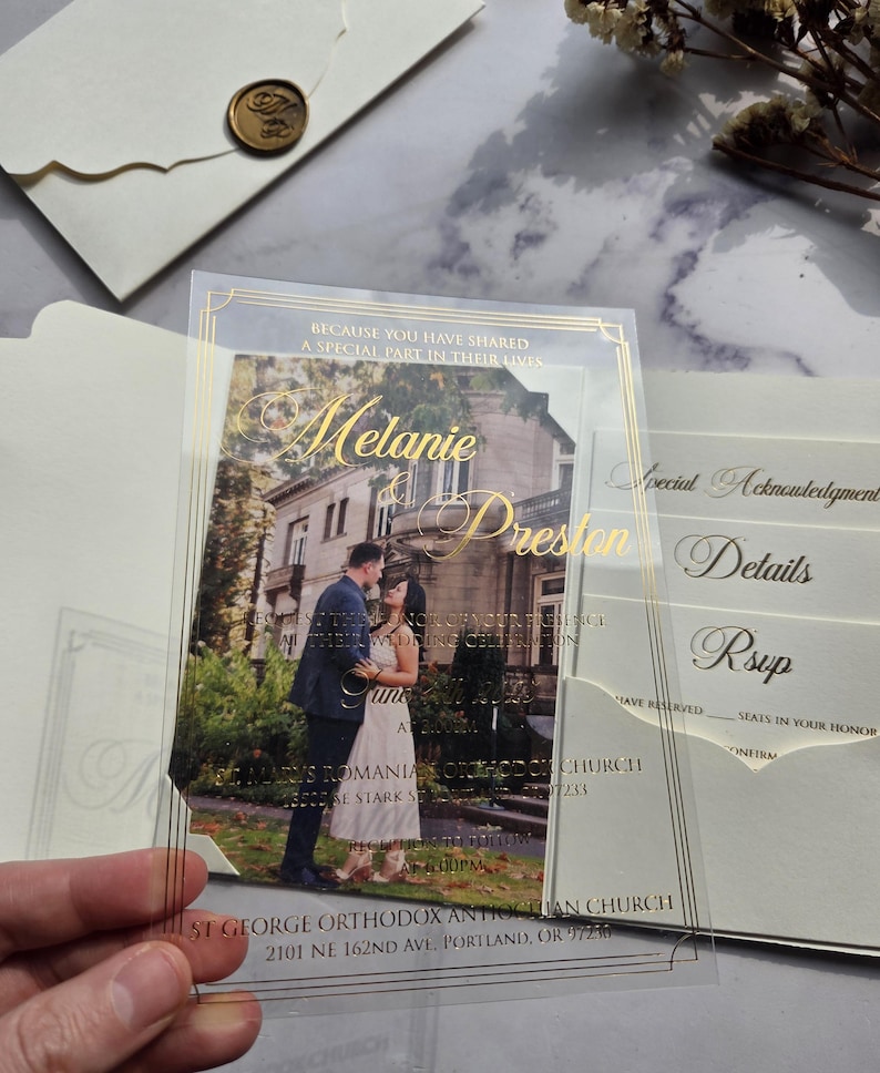 May include: A clear acrylic wedding invitation with gold foil accents. The invitation features a photo of a couple in front of a building. The text on the invitation reads "Because you have shared a special part in their lives, Melanie & Preston".