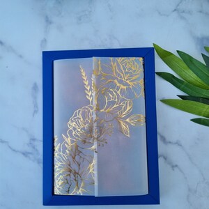 May include: A rectangular blue card holder or frame featuring a translucent vellum overlay. The vellum is decorated with a metallic gold floral line art design, showcasing detailed illustrations of blooming flowers and foliage on the front surface.