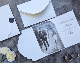 Puede incluir: Conjunto de invitaciones de boda blancas con bordes festoneados, con una foto de una pareja y detalles. Incluye un sello de cera negro en un sobre y dos anillos de boda dorados. El texto dice "Lindsey Mongan Thomas Soofield".
