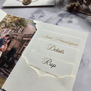 May include: A white wedding invitation with a gold foil design. The invitation has a pocket for a RSVP card. The text on the invitation reads "Special Acknowledgment", "Details", and "Rsvp".