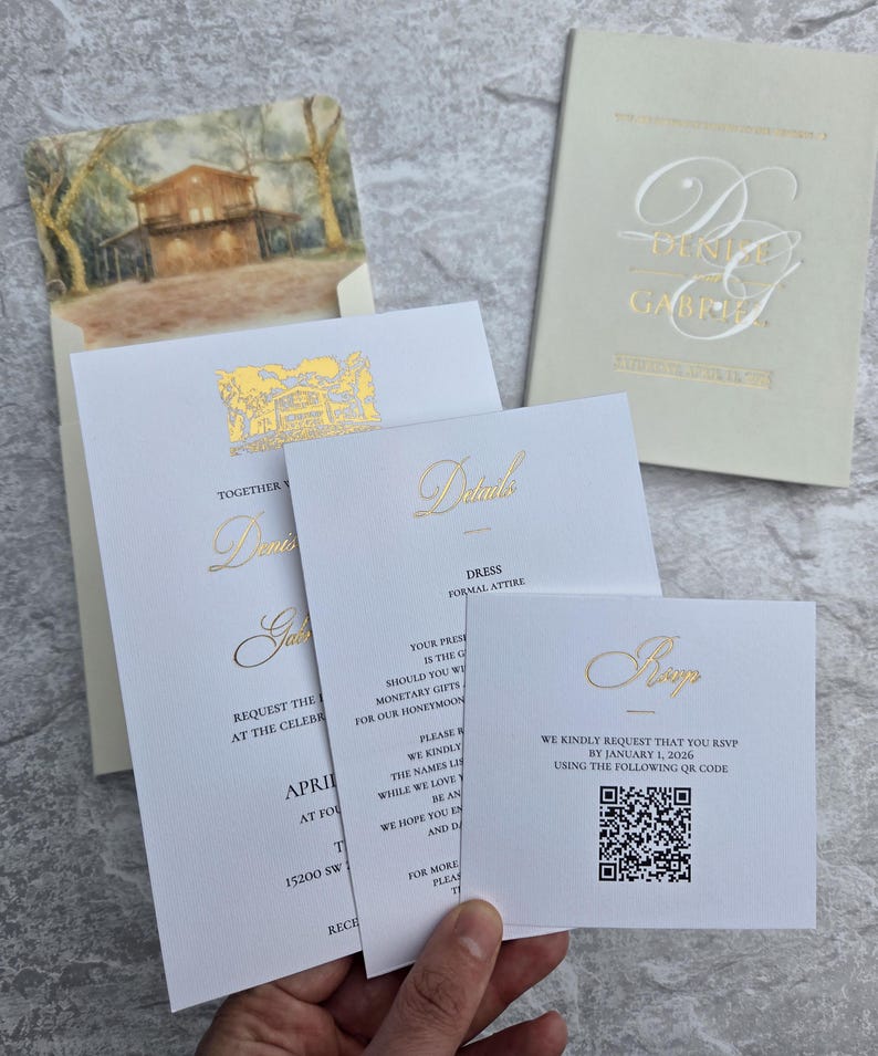 K&ouml;nnte beinhalten: Hochzeitseinladungs-Set mit goldfarbenem Folienschriftzug auf wei&szlig;em und cremefarbenem Karton. Enth&auml;lt Einladungs-, Detail- und RSVP-Karten. Die Einladung zeigt die Namen "Denis & Gabriel". Die RSVP-Karte enth&auml;lt einen QR-Code.