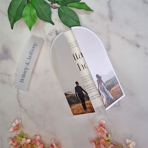 Può includere: Un invito di nozze bianco con una foto di una sposa e uno sposo in un campo. L'invito è piegato a metà e ha un arco arrotondato in alto. Il testo sull'invito recita "Brittany & Anthony" e "Il ventidue giugno duemilaventitré, alle quattro del pomeriggio."