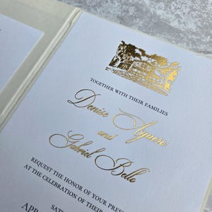 K&ouml;nnte beinhalten: Eine Hochzeitseinladung mit goldfarbenen Buchstaben und einer goldenen Illustration eines Geb&auml;udes. Die Einladung enth&auml;lt die Namen "Denise" und "Aguero" und "Gabriel Belle" sowie das Datum "11. April". Der Text lautet: "Bitten Sie um die Ehre Ihrer Anwesenheit bei der Feier ihrer Hochzeit."