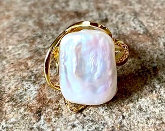 May include: A gold-toned ring featuring a large, rectangular, iridescent white pearl with a textured surface. The metal band has an open, organic, and asymmetrical design that wraps around the base of the central pearl setting.