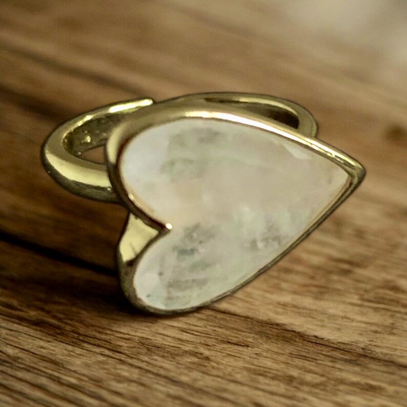 Puede incluir: Un anillo de oro con una piedra preciosa blanca en forma de coraz&oacute;n. El anillo est&aacute; sobre una superficie de madera.