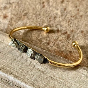 May include: A gold bangle bracelet with a row of small, dark gray pyrite stones set into the band.