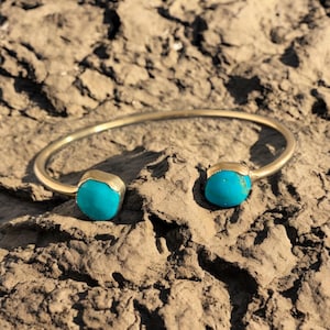 May include: A gold bangle bracelet with two turquoise stones on either end.
