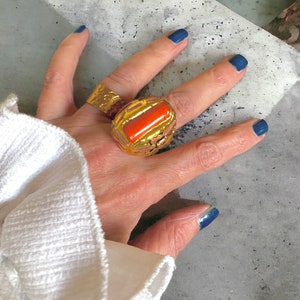 May include: A gold ring with a large, rectangular, orange stone set in a textured gold frame.