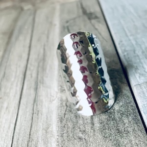 May include: A silver hammered ring with a textured surface. The ring is wide and has a slightly curved shape.