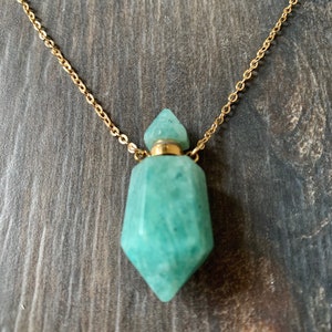 Może przedstawiać: Złoty łańcuszek z zielonym kamieniem szlachetnym w kształcie butelki. Butelka ma złoty korek i fasetowany wzór.