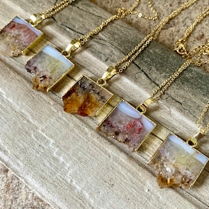 May include: Five gold necklaces with square pendants featuring different shades of brown, orange, and white crystal clusters.