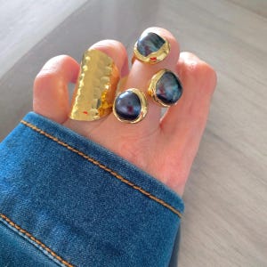 May include: Three gold rings with black pearl stones. The rings are worn on a hand with a denim sleeve.