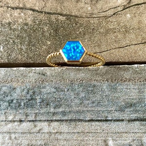 May include: A gold ring with a blue hexagonal gemstone. The ring has a twisted band.