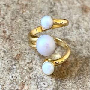 May include: A gold ring with three white pearl-like stones set in a spiral design.
