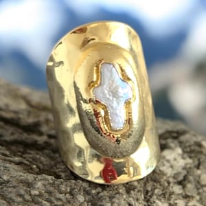 May include: Gold ring with a hammered finish and a white cross inlay.