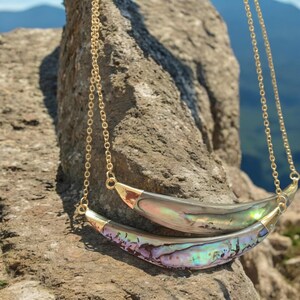 May include: A gold chain necklace with two iridescent abalone shell pendants in the shape of a crescent moon.