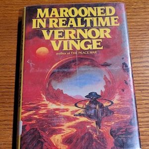 May include: A paperback book titled "Marooned in Realtime" by Vernor Vinge. The cover art features a science fiction scene with a red and orange planet, a futuristic vehicle, and the author's name in yellow text.
