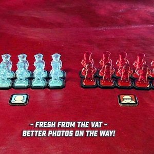 May include: Two rows of miniature plastic figures, one row of 10 red figures and one row of 10 blue figures. The figures are arranged in a line on a red surface. The text "FRESH FROM THE VAT - BETTER PHOTOS ON THE WAY!" is printed below the figures.