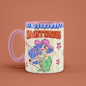 May include: A ceramic mug with a pink handle and rim, featuring a Sagittarius design. The design includes a woman with blue hair, a pink hat, and a bow and arrow, with the word "SAGITTARIUS" in orange letters.
