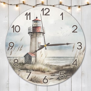 Puede incluir: Un reloj redondo con fondo blanco y números negros. La esfera del reloj presenta una pintura de acuarela de un faro en una playa con olas y gaviotas. Las manecillas del reloj son negras.