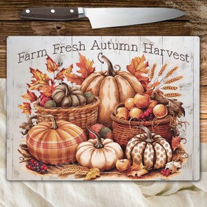 Puede incluir: Tabla de cortar rectangular con temática de cosecha de otoño. Presenta calabazas, manzanas y cestas, con el texto "Farm Fresh Autumn Harvest". Un cuchillo de acero inoxidable con mango marrón descansa encima.