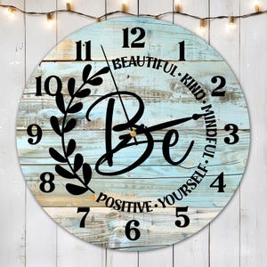 Könnte beinhalten: Eine runde Holzuhr mit einem blauen und weißen, abgenutzten Holzhintergrund. Das Zifferblatt der Uhr hat schwarze römische Ziffern und ein schwarzes Blumenmuster. Die Worte "Be Beautiful. Kind. Mindful. Positive. Yourself." sind um das Zifferblatt der Uhr geschrieben.