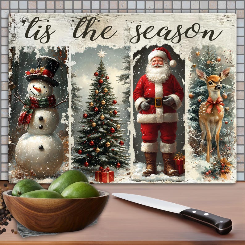 May include: A festive Christmas-themed cutting board with the text "'tis the season." The board features a snowman, Christmas tree, Santa Claus, and a deer. A wooden bowl of green fruit and a knife are in the foreground.