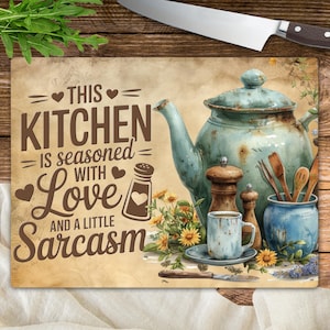May include: A rectangular cutting board with a vintage design. The board features a teal teapot, a coffee cup, and the text "THIS KITCHEN IS SEASONED WITH LOVE AND A LITTLE SARCASM." A knife and utensils are also visible.