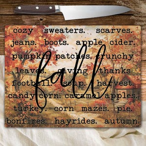 Può includere: Un tagliere rettangolare con un design a tema autunnale, con la parola "fall" in grandi caratteri. La tavola include parole legate all'autunno come "pumpkin patches" e "hayrides". Un coltello è appoggiato in cima.