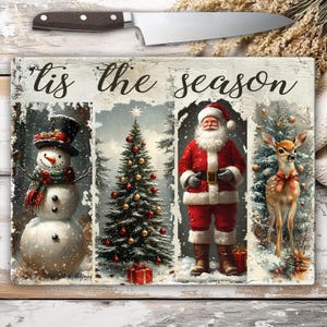 May include: A rectangular cutting board with a festive Christmas design. The board features a snowman, Christmas tree, Santa Claus, and a deer, with the text "'Tis the season". A knife rests above the board.