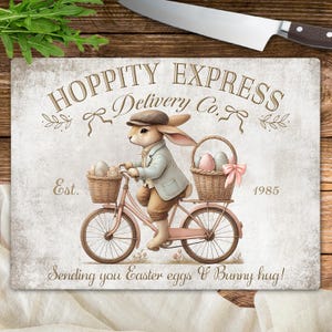 May include: A vintage-style illustration of a bunny riding a bicycle with baskets full of Easter eggs. The text reads "Hoppity Express Delivery Co. Est. 1985" and "Sending you Easter eggs & Bunny hug!"