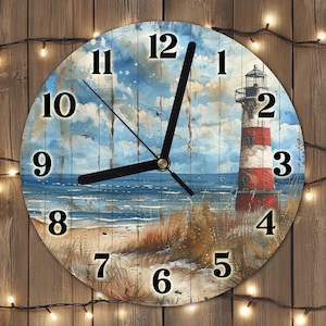 Op de afbeelding: Ronde wandklok met een kustontwerp, met een vuurtoren, strand en zee. De wijzerplaat heeft zwarte cijfers en wijzers. De vuurtoren is rood en wit. De achtergrond is een aquarel schilderij van een blauwe lucht en oceaan.