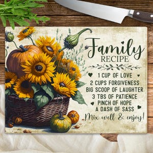 May include: Rectangular cutting board with a floral and pumpkin design. The board features a basket of sunflowers and pumpkins, with the text "Family Recipe" and a list of ingredients. The board is on a wooden surface.