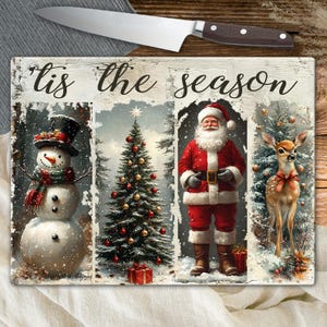 May include: A rectangular cutting board with a festive winter scene. The board features a snowman, Christmas tree, Santa Claus, and a deer. The words "'Tis the season" are written across the top. A stainless steel knife with a brown handle rests above the board.