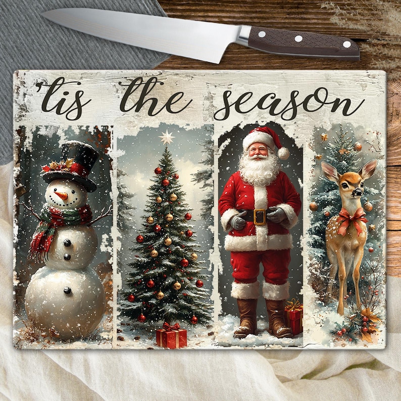 May include: A rectangular cutting board with a festive winter scene. The board features a snowman, Christmas tree, Santa Claus, and a deer. The words "'Tis the season" are written across the top. A stainless steel knife with a brown handle rests above the board.