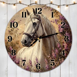 Puede incluir: Un caballo blanco con una brida negra y ojos marrones se representa en una esfera de reloj redonda con marcadores de hora en números romanos y agujas negras. El fondo presenta un diseño floral con flores moradas.