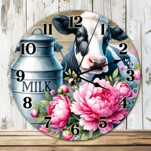 Puede incluir: Un reloj de pared redondo con una vaca en blanco y negro con una nariz rosa, rodeada de peonías rosas y hojas verdes. A la izquierda hay una jarra de leche de metal. La esfera del reloj tiene números y manecillas negras.