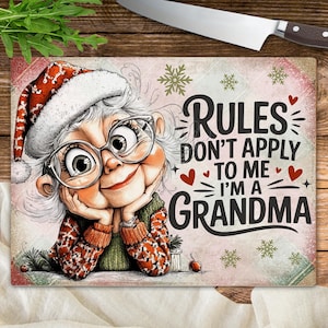 Puede incluir: Tabla de cortar rectangular con una imagen de dibujos animados de una abuela sonriente con gorro de Papá Noel y gafas. El texto dice "RULES DON'T APPLY TO ME I'M A GRANDMA". La tabla tiene un borde rojo y blanco.