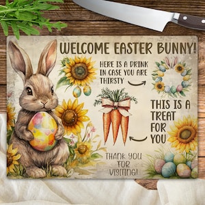 May include: A welcome Easter bunny chopping board featuring a brown bunny rabbit holding a colourful Easter egg. The board has a sunflower design and the text "Welcome Easter Bunny! Here is a drink in case you are thirsty. This is a treat for you. Thank you for visiting!"