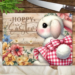 May include: A white bunny wearing a red and white gingham dress with a bow. The bunny is on a wooden background with flowers and the text "Hoppy Easter".