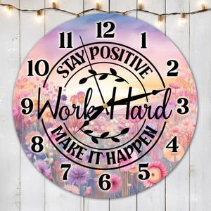 Könnte beinhalten: Eine runde Uhr mit einem Blumendesign und dem Text "Stay Positive Work Hard Make It Happen". Das Zifferblatt der Uhr hat schwarze Zahlen und Zeiger.