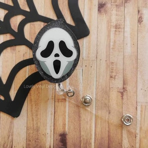 Peut inclure: Un porte-badge rétractable noir et blanc avec un visage de fantôme noir et blanc sur fond de paillettes.  "Lovely Vinyl Designs" est imprimé sur le porte-badge.