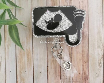 May include: Silver glitter badge reel with a black background featuring a silver glitter ultrasound image of a baby. The text "Lovely Vinyl Designs" is printed below the image.